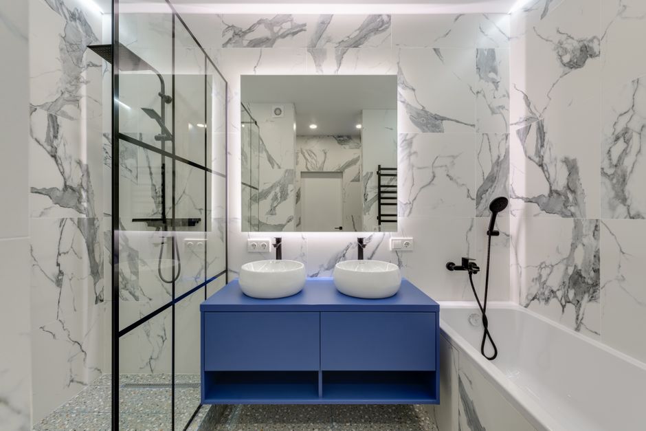 Modern bathroom interior featuring marble walls, dual sinks, and a glass shower.
