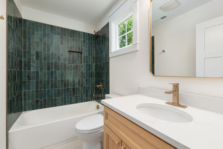 Elegant bathroom featuring a green tiled wall, white tub, and wooden vanity with gold fixtures
